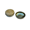 Two small oval cosmetic or accessory containers displayed on a white circular stand against a textured blue-gray background.