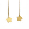 A pair of long gold chain earrings with small flower-shaped pendants, hanging against a plain light gray wall. 14K gold filled