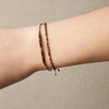 OLIVE bracelet layered on the wrist, showing faceted olive-bronze beads and braided gold-threaded cord.