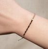 SABLE black spinel and 9k solid gold bracelet worn on the wrist, showing its delicate beadwork and braided taupe thread.