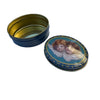 A round decorative tin with a dark blue exterior and gold interior, shown open next to its matching lid featuring a classical cherub illustration on a light blue background.