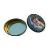 An oval metal tin with its lid off, resting on a white circular stand. The lid features a decorative illustration of cherubs on a blue background with gold detailing, and the inside of the tin is lined with a pale mint green material.