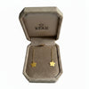 A pair of gold flower-shaped dangle earrings displayed inside an open beige KEKE jewelry box on a light gray textured background. 