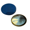 Two oval metal cosmetic tins, one dark blue and one gold-toned, displayed on a white circular stand against a gray textured background.